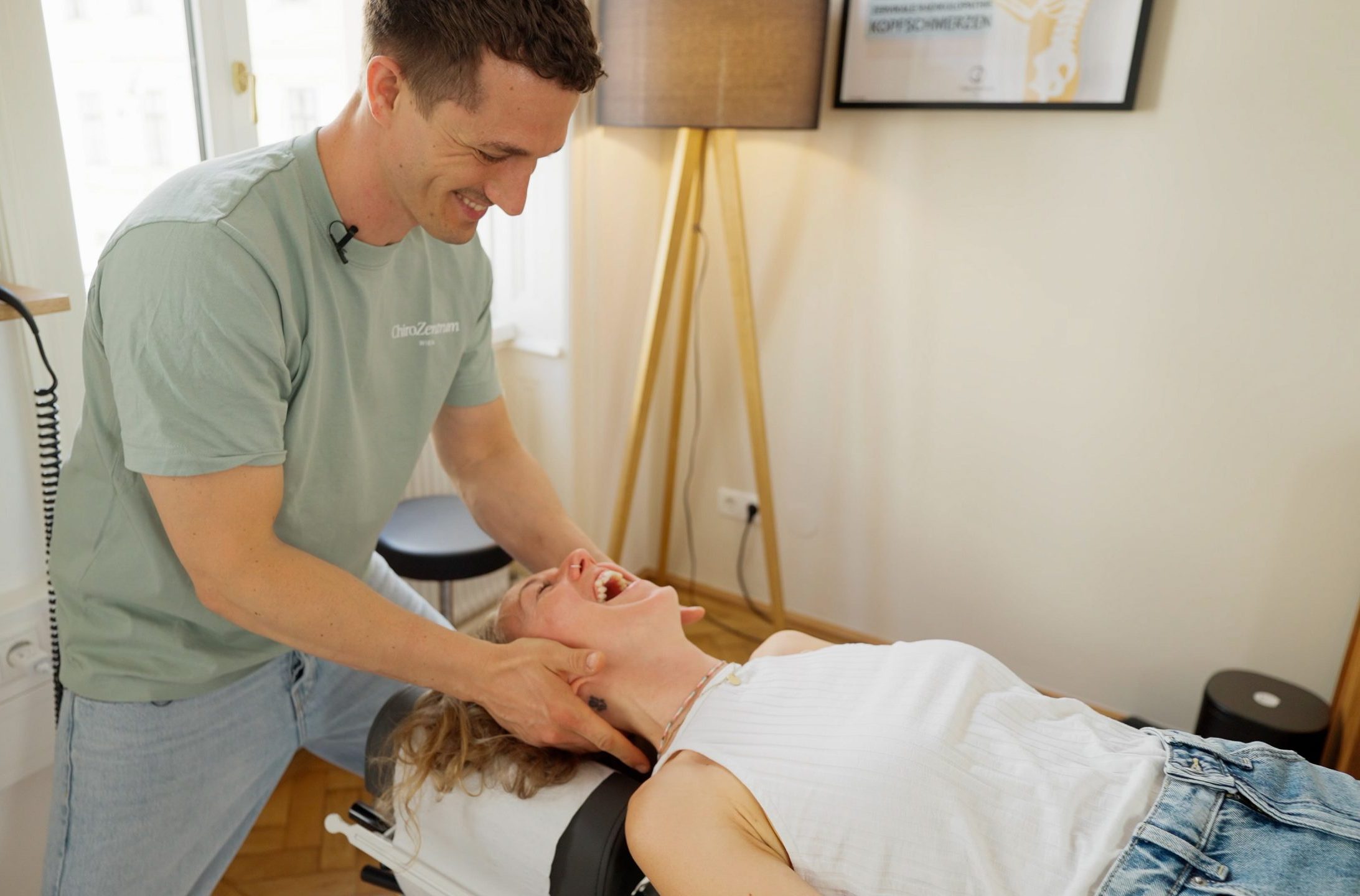 Felix Trescher und eine Patientin lachen während einer Chiropraktik Behandlung im ChiroZentrum Wien.